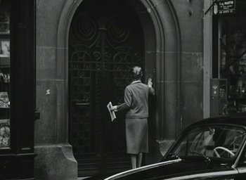 Movie still from “Elevator to the Gallows” (1958), directed by Louis Malle – A woman holding a newspaper while standing in front of a building; Wide shot, High angle