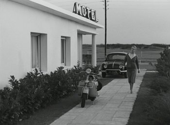 Movie still from “Elevator to the Gallows” (1958), directed by Louis Malle – A woman walking down a sidewalk next to a motor scooter; Wide shot, Low angle