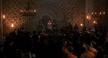 Movie still from “Elizabeth” (1998), directed by Shekhar Kapur – A group of people sitting in front of an ornate wall; Wide shot, High angle
