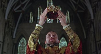 Movie still from “Elizabeth” (1998), directed by Shekhar Kapur – A man holding a crown up in the air in front of stained glass windows; Close Up shot, Low angle