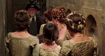 Movie still from “Elizabeth” (1998), directed by Shekhar Kapur – A group of people in renaissance costumes looking at an old man; Medium shot, Over the shoulder angle