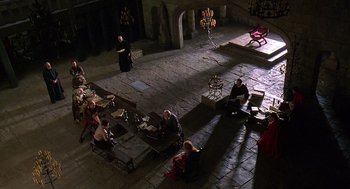 Movie still from “Elizabeth” (1998), directed by Shekhar Kapur – A group of people sitting on benches in a room; Extreme Wide shot, High angle