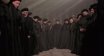 Movie still from “Elizabeth” (1998), directed by Shekhar Kapur – A group of men in black robes standing in a room; Wide shot, High angle