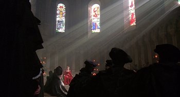 Movie still from “Elizabeth” (1998), directed by Shekhar Kapur – A group of people sitting in front of stained glass windows in a church; Wide shot, Low angle