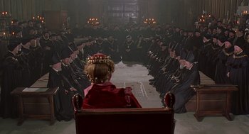 Movie still from “Elizabeth” (1998), directed by Shekhar Kapur – A group of people sitting in a room with a little girl sitting on a bench in front of them; Wide shot, High angle