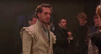 Movie still from “Elizabeth” (1998), directed by Shekhar Kapur – A man wearing a suit and tie standing in front of other men; Close Up shot, Over the shoulder angle