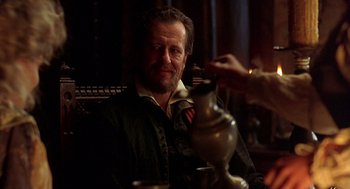 Movie still from “Elizabeth” (1998), directed by Shekhar Kapur – A man sitting in front of a table holding a fork; Medium shot, Over the shoulder angle