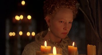Movie still from “Elizabeth” (1998), directed by Shekhar Kapur – A woman in a white dress with three lit candles in front of her face; Close Up shot, Over the shoulder angle