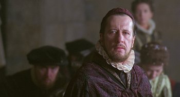 Movie still from “Elizabeth” (1998), directed by Shekhar Kapur – A person with a beard wearing a hat; Close Up shot, Over the shoulder angle