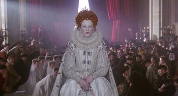 Movie still from “Elizabeth” (1998), directed by Shekhar Kapur – A woman dressed as queen elizabeth in front of an audience; Medium shot, High angle