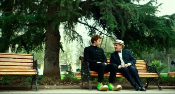 Two men sitting on a park bench next to a tree