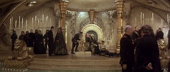 Movie still from “Dune” (1984), directed by David Lynch – A group of people sitting on a stage in front of a throne; Wide shot, High angle