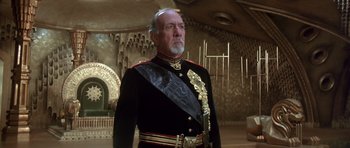 Movie still from “Dune” (1984), directed by David Lynch – An older man in a military uniform stands in front of a wall; Medium shot, Low angle