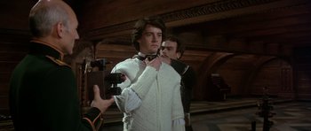 Movie still from “Dune” (1984), directed by David Lynch – A man in a white sweater tying a bow tie; Medium shot, Over the shoulder angle