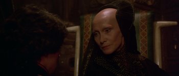 Movie still from “Dune” (1984), directed by David Lynch – An older woman with a bald head and long hair; Close Up shot, Over the shoulder angle