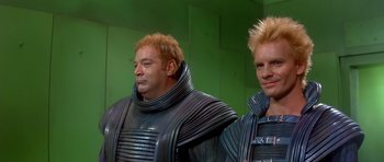 Movie still from “Dune” (1984), directed by David Lynch – Two men in black suits standing next to each other; Medium shot, Low angle