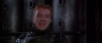 Movie still from “Dune” (1984), directed by David Lynch – A man in a black rubber suit smiling for the camera; Close Up shot, Low angle