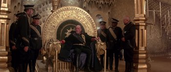 Movie still from “Dune” (1984), directed by David Lynch – A man sitting on top of a throne next to two other men; Wide shot, Low angle