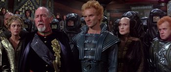 Movie still from “Dune” (1984), directed by David Lynch – A group of people in costume in a room; Medium shot, Over the shoulder angle
