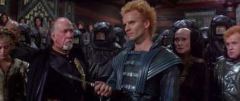 Movie still from “Dune” (1984), directed by David Lynch – A group of people in costume in a room; Medium shot, Over the shoulder angle