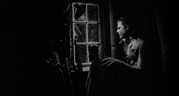 Movie still from “Eraserhead” (1977), directed by David Lynch – A black and white photo of a man sitting in front of a window; Medium shot, Low angle