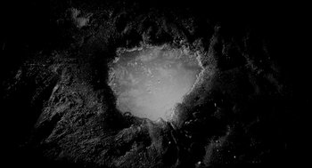 Movie still from “Eraserhead” (1977), directed by David Lynch – A black - and - white photo of a crater on the surface of the moon; Extreme Wide shot, Overhead angle