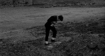Movie still from “Eraserhead” (1977), directed by David Lynch – A man standing in the dirt with his head in his hands; Wide shot, High angle