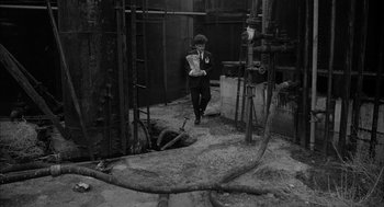 Movie still from “Eraserhead” (1977), directed by David Lynch – A man in a suit and tie standing in an alley; Wide shot, High angle