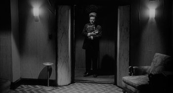 Movie still from “Eraserhead” (1977), directed by David Lynch – A woman standing in front of a mirror in a room; Wide shot, Low angle
