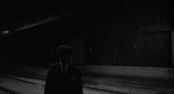 Movie still from “Eraserhead” (1977), directed by David Lynch – A man standing in front of train tracks at night; Wide shot, Low angle