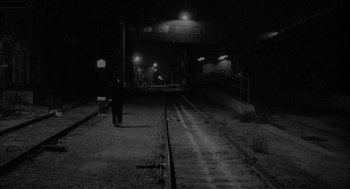 Movie still from “Eraserhead” (1977), directed by David Lynch – A man standing on a train track at night; Extreme Wide shot, High angle