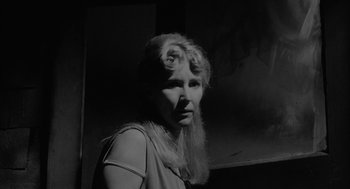 Movie still from “Eraserhead” (1977), directed by David Lynch – A black and white photo of a woman in front of a painting; Close Up shot, Low angle