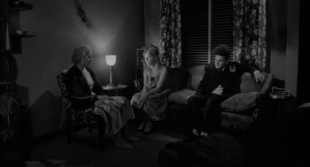 Movie still from “Eraserhead” (1977), directed by David Lynch – A group of people sitting in a living room next to each other; Wide shot, Over the shoulder angle