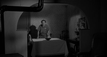 Movie still from “Eraserhead” (1977), directed by David Lynch – A man standing at a table with a bowl in front of him; Wide shot, High angle