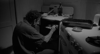 Movie still from “Eraserhead” (1977), directed by David Lynch – A man sitting in front of an open oven; Medium shot, High angle