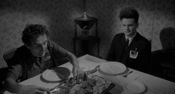 Movie still from “Eraserhead” (1977), directed by David Lynch – Two men sitting at a table with a plate of food on it; Medium shot, Over the shoulder angle