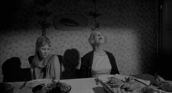 Movie still from “Eraserhead” (1977), directed by David Lynch – Two women sitting at a dinner table looking up at the sky; Medium shot, Low angle