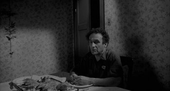 Movie still from “Eraserhead” (1977), directed by David Lynch – A black and white photo of a man sitting at a dinner table; Medium shot, Over the shoulder angle