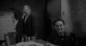 Movie still from “Eraserhead” (1977), directed by David Lynch – An older woman standing next to an older man in a room; Medium shot, Over the shoulder angle