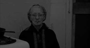 Movie still from “Eraserhead” (1977), directed by David Lynch – An older woman with glasses smoking a cigarette; Close Up shot, Over the shoulder angle