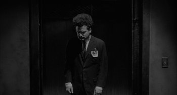 Movie still from “Eraserhead” (1977), directed by David Lynch – A black and white photo of a man in a suit and tie; Medium shot, Low angle