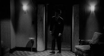 Movie still from “Eraserhead” (1977), directed by David Lynch – A black and white photo of a man in a suit and tie; Wide shot, High angle