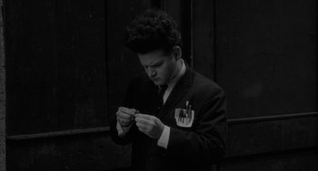 Movie still from “Eraserhead” (1977), directed by David Lynch – A man in a suit and tie looking down at a piece of paper in his hands; Medium shot, High angle