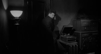 Movie still from “Eraserhead” (1977), directed by David Lynch – A man standing in front of an old record player; Medium shot, High angle
