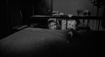 Movie still from “Eraserhead” (1977), directed by David Lynch – A young girl leaning against a metal railing in a room; Wide shot, High angle