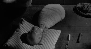 Movie still from “Eraserhead” (1977), directed by David Lynch – A baby wrapped in a blanket laying on a bed; Close Up shot, High angle