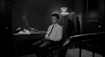 Movie still from “Eraserhead” (1977), directed by David Lynch – A man sitting in a chair in front of a desk; Medium shot, High angle