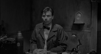 Movie still from “Eraserhead” (1977), directed by David Lynch – A black and white photo of a man sitting at a table; Medium shot, High angle