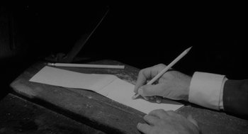 Movie still from “Eraserhead” (1977), directed by David Lynch – A person writing on a piece of paper with a pencil; Extreme Close Up shot, High angle