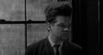Movie still from “Eraserhead” (1977), directed by David Lynch – A black and white photo of a man with a messy hair style; Close Up shot, Over the shoulder angle